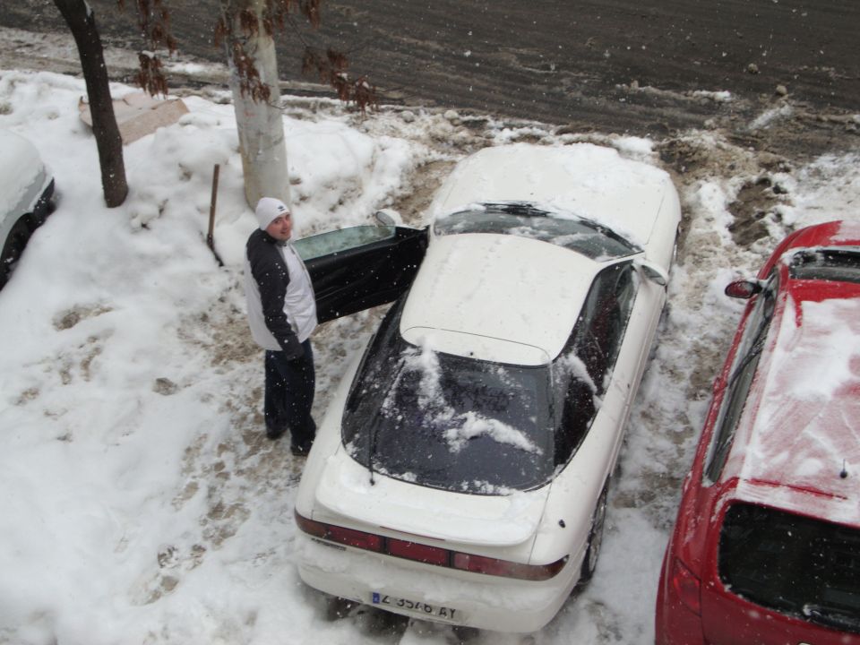 White coupe with door open in snow, parked next to a red car
