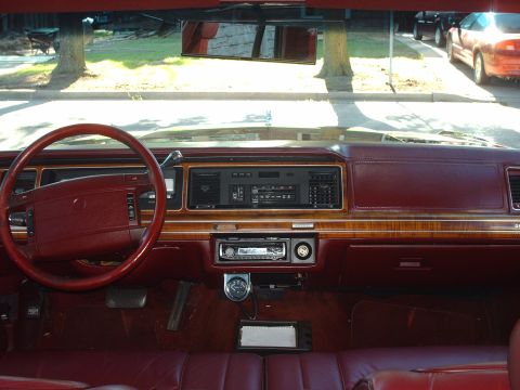 1991 Mercury Grand Marquis - The dashboard and steering wheel of a car are shown, wood grain accents and a maroon interior.