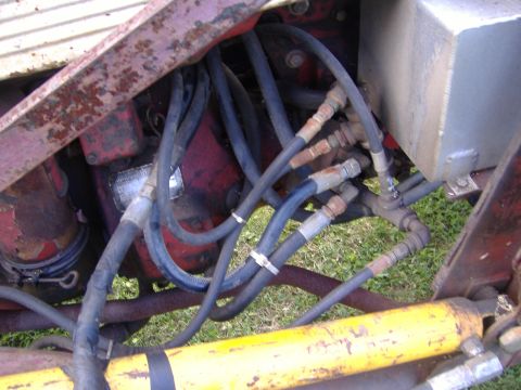 1988 Ford Bronco - Hydraulic hoses and engine components are visible on a red tractor, with a yellow cylinder in the foreground.