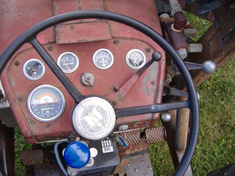 Tractor dashboard showing oil, water temp, and amp gauges, plus an hour meter. Steering wheel and control levers are visible