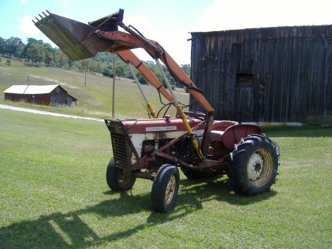 1988 Ford Bronco - A red and white tractor equipped with a front loader sits in a grassy field next to a weathered wooden barn.