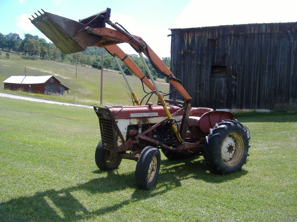 Red and white tractor with front loader parked in a grassy field