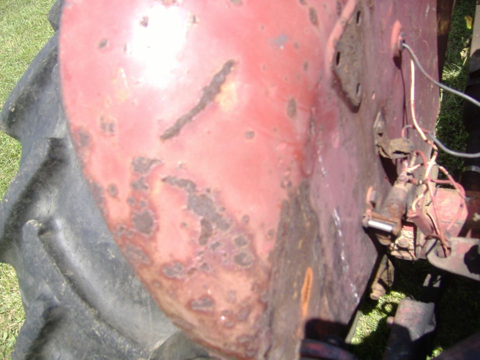 Close-up of a red tractor fender with rust spots next to a large tire