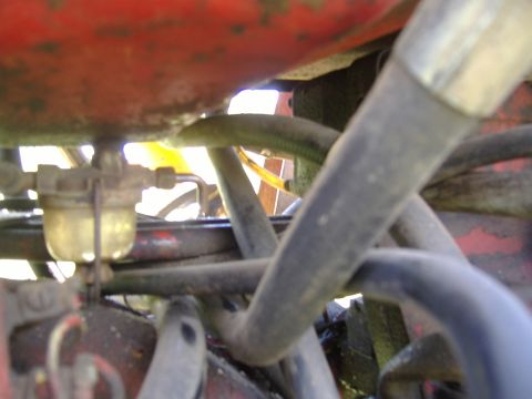 1988 Ford Bronco - Tight view under the hood or fuel tank of an old red machine showing a glass-bowl sediment fuel filter mounted to a casting, surrounded by…