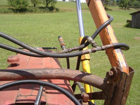 1988 Ford Bronco - Hydraulic lines connect to the loader arm of a tractor, with a grassy field and trees in the background.