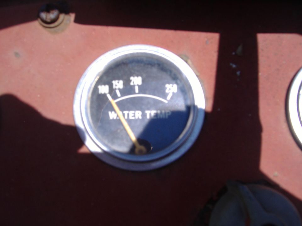 Water temperature gauge with needle pointing to 100 degrees, set in a dark red dashboard