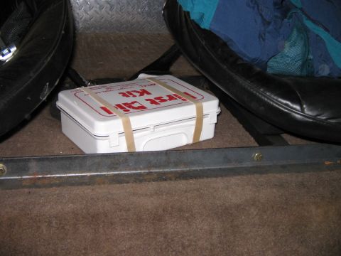 1992 Ford Bronco - A white first aid kit is secured with rubber bands on the floor of a vehicle's interior.
