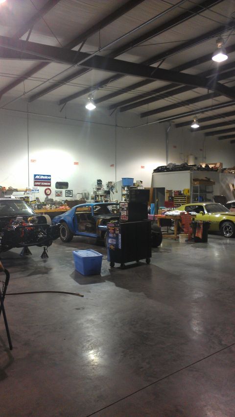 1973 Chevrolet Camaro - Multiple vehicles are undergoing repairs and restoration in a large workshop setting.