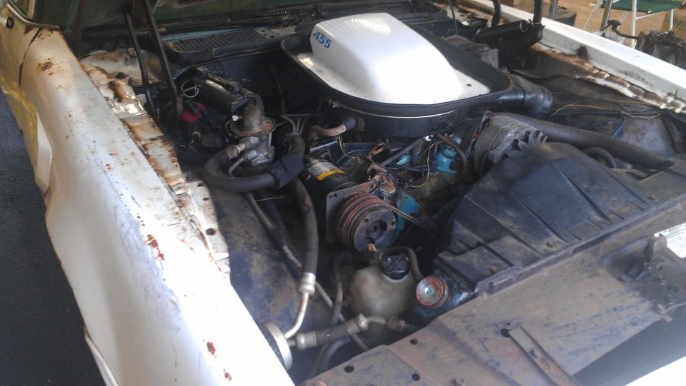 Engine bay of a car, showing the engine, air cleaner with '455' label, and various hoses and components. Some rust is visible on the fender