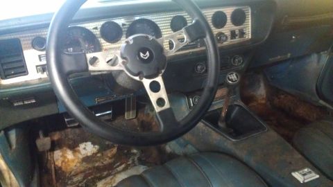 1973 Chevrolet Camaro - The interior of a classic Pontiac Firebird, an aftermarket steering wheel and worn upholstery.