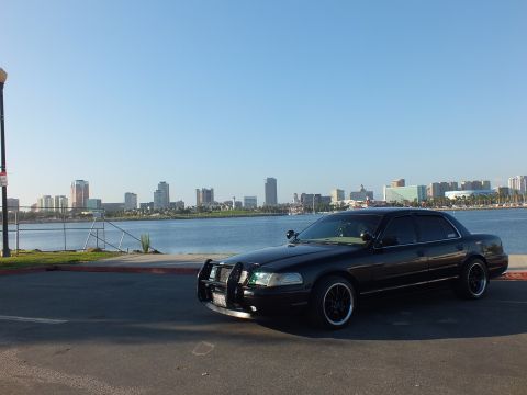 2003 Ford Crown Victoria - Blacked-out sedan sits by the marina as a city skyline rises across the water