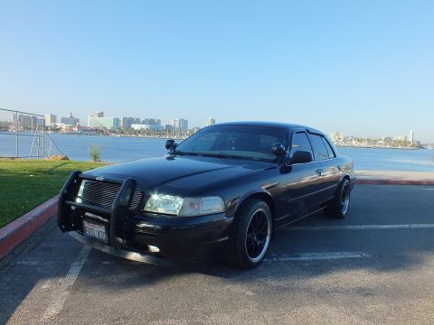 2003 Ford Crown Victoria - Blacked-out sedan with brush guard parked by harbor, front California plate shown