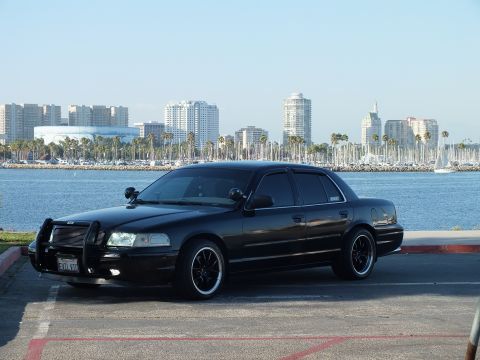 2003 Ford Crown Victoria - Murdered-out sedan sits curbside as boats and city towers line the harbor