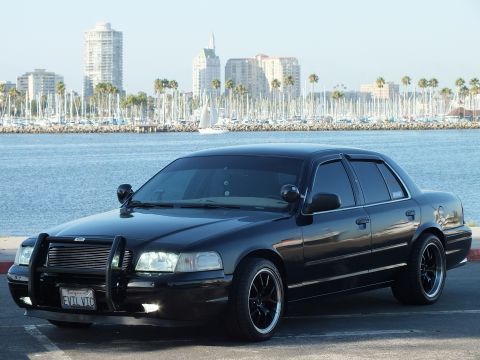 2003 Ford Crown Victoria - Blacked-out sedan with vanity plate EVIL VIC parked before harbor and skyline