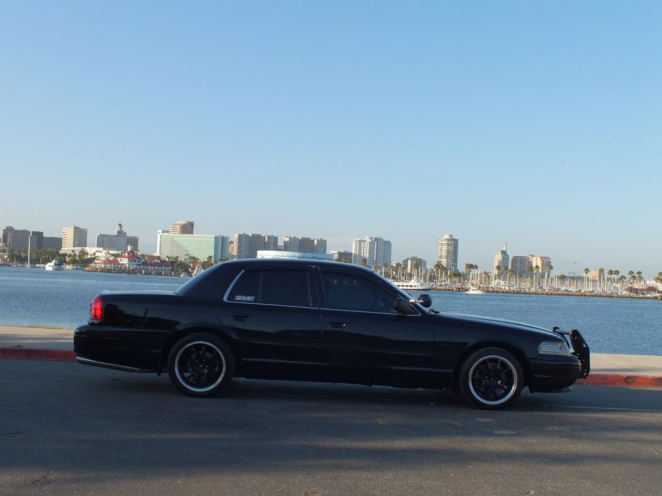 Side profile of blacked-out Ford Crown Victoria sedan on black wheels at Long Beach harbor