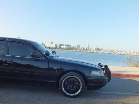 2003 Ford Crown Victoria - Close front-three-quarter view of a lowered black sedan with push bar, harbor and high-rises behind