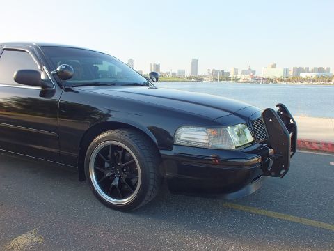 2003 Ford Crown Victoria - Tight detail of a blacked-out sedan's nose and push bar, marina and skyline in the background