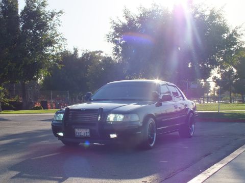 2003 Ford Crown Victoria - Front-three-quarter of a lowered blacked-out sedan with grille guard under heavy sun glare