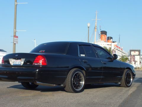 2003 Ford Crown Victoria - Lowered blacked-out Ford sedan rear view, SVT-style badge, with the Queen Mary docked beyond