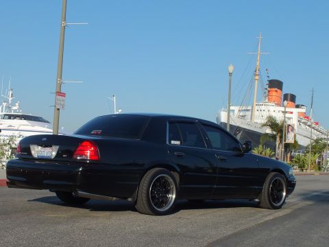 2003 Ford Crown Victoria - Murdered-out Ford sedan from behind with the Queen Mary liner and palms in the background