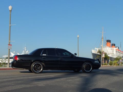 2003 Ford Crown Victoria - Profile of a murdered-out sedan parked along the waterfront with the Queen Mary in view