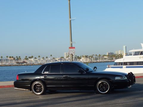 2003 Ford Crown Victoria - Murdered-out sedan with grille guard parked along the water with a yacht and palms behind
