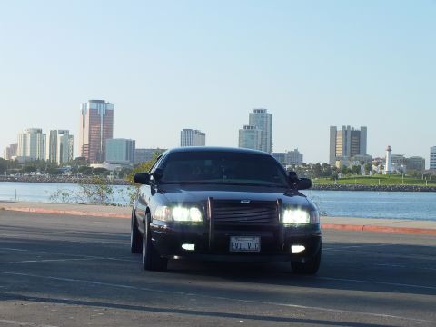 2003 Ford Crown Victoria - Front view of a murdered-out sedan with push bar and lit headlights against the skyline