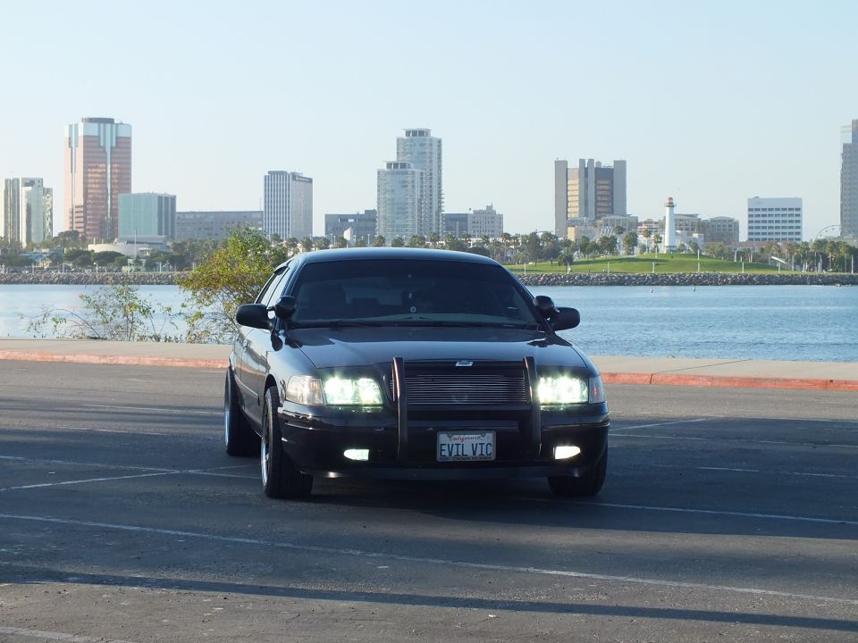 Black Ford Crown Victoria with grille guard and lit lights, EVIL VIC plate, Long Beach skyline