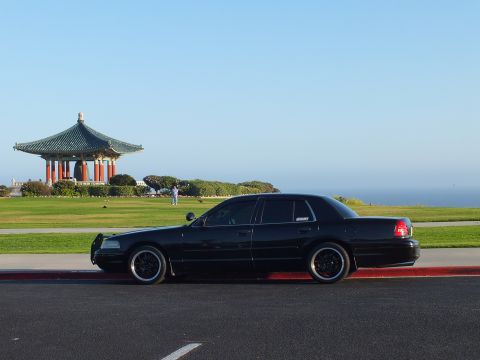 2003 Ford Crown Victoria - Side view of a lowered black four-door against a clear sky, hilltop pagoda and sea behind.