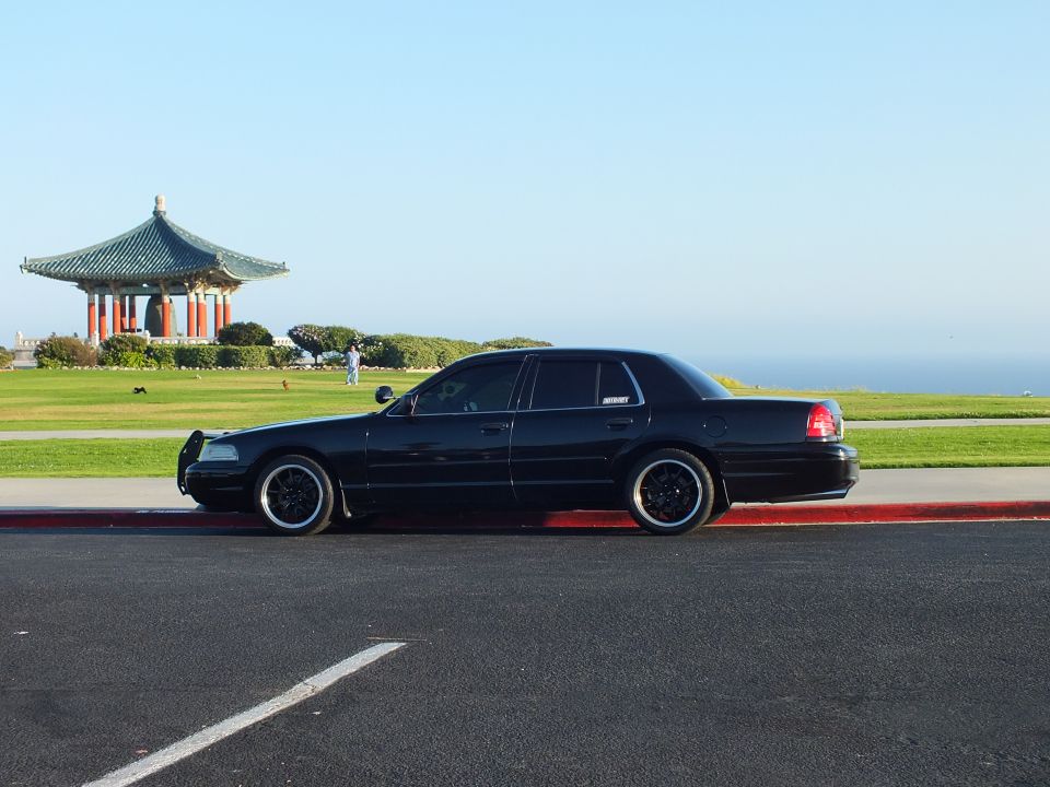 Black full-size sedan profile on gloss-black wheels by ocean overlook and pagoda