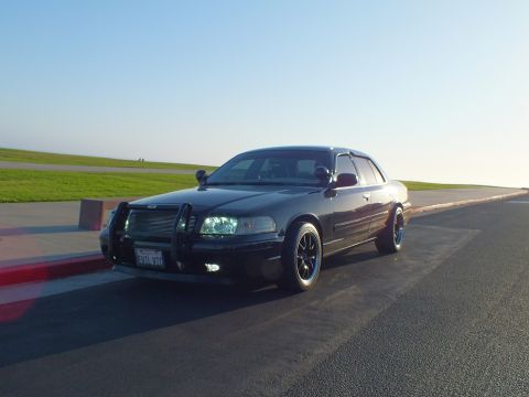 2003 Ford Crown Victoria - Front three-quarter of a black four-door with grille guard and dark wheels, sea horizon beyond.