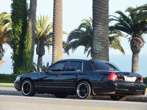 2003 Ford Crown Victoria - Lowered black sedan shot from behind, ocean and palms framing the roadside.