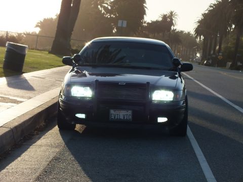 2003 Ford Crown Victoria - Crown Victoria front end, black mesh grille and California EVIL VIC plate at curb.