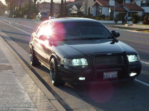 2003 Ford Crown Victoria - Crown Victoria with push bar parked curbside, houses across a coastal street.