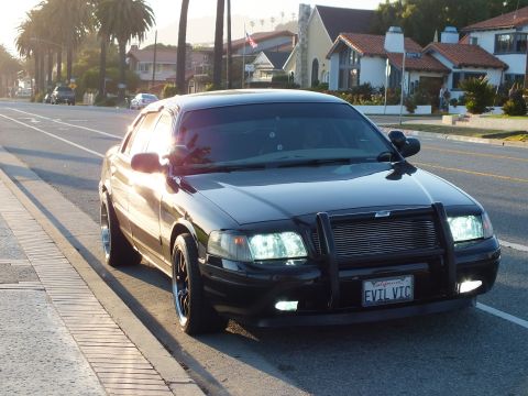 2003 Ford Crown Victoria - Blacked-out Crown Victoria with brush guard, Spanish-style homes in background.