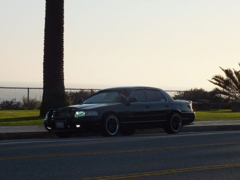 2003 Ford Crown Victoria - Crown Victoria with push bar at the curb, ocean and palms in soft evening light.