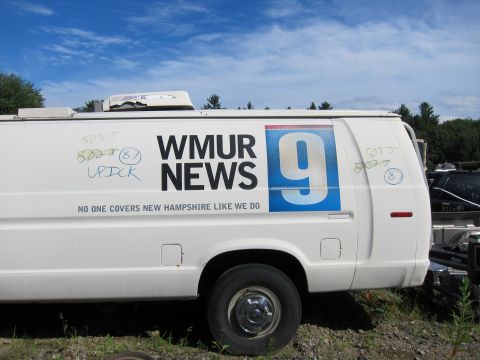 1991 Ford LTD Crown Victoria - WMUR News van with graffiti, parked outdoors under a blue sky with clouds.