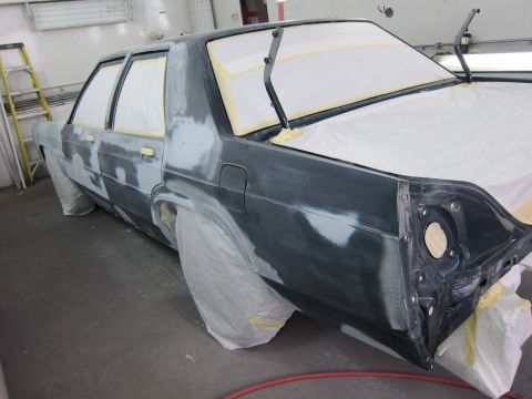 1991 Ford LTD Crown Victoria - A dark sedan, likely a Ford Crown Victoria, is in a body shop for repairs, with windows and parts covered.