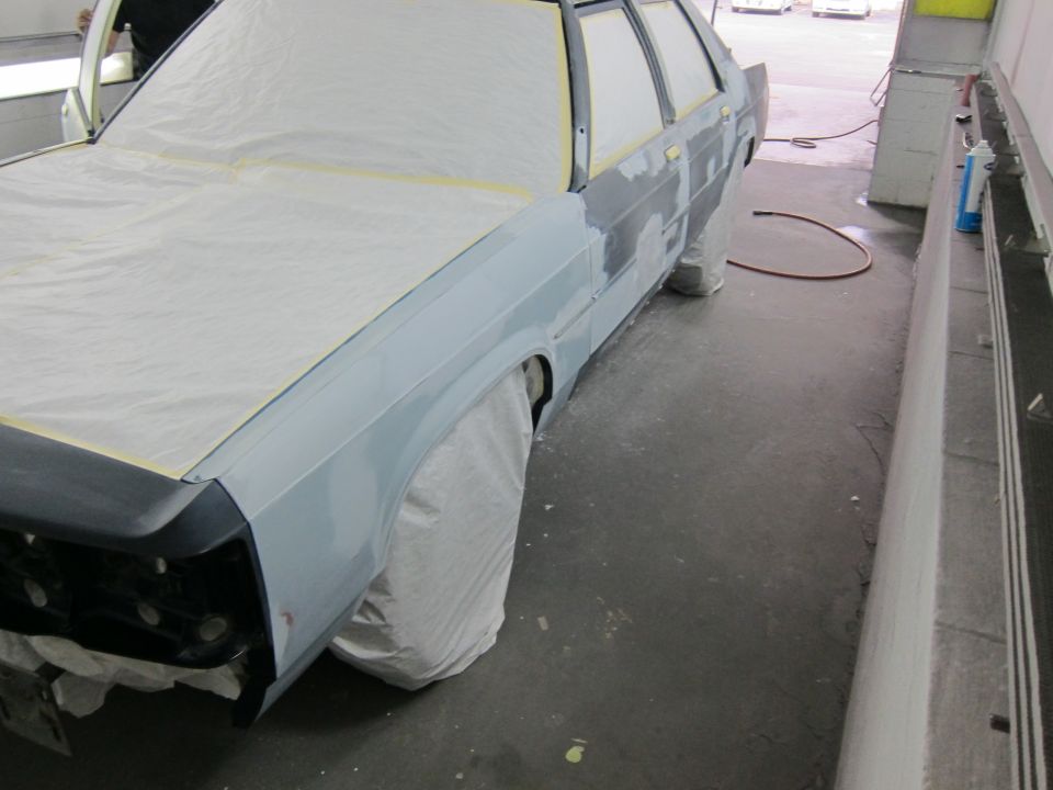 Car body covered in plastic, undergoing prep work in a garage