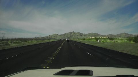 1985 Toyota 4Runner - A white SUV travels down a highway through a vast desert landscape under a cloudy sky.