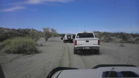 1985 Toyota 4Runner - A convoy of vehicles travels down a dusty desert trail under a clear blue sky.