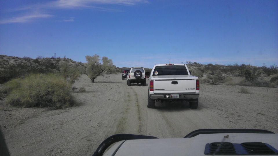 White pickup truck and two SUVs driving on a dirt road in a desert landscape