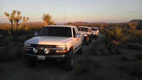 1985 Toyota 4Runner - A convoy of trucks travels through a desert landscape as the sun sets, casting long shadows.