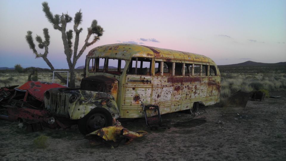 Yellow bus and red car wreckage in desert landscape with Joshua trees