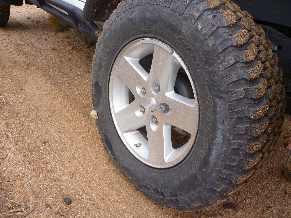 Close-up of a silver five-spoke wheel with a knobby tire on sandy terrain