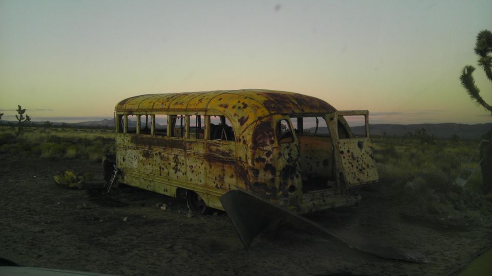 Yellow school bus, heavily rusted, doors open, in a desert landscape