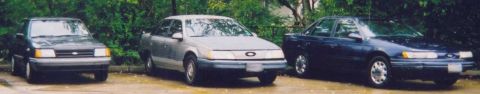 1989 Ford Escort - Three sedans are parked outdoors, with the leftmost vehicle appearing to be a 1986 Ford Taurus.