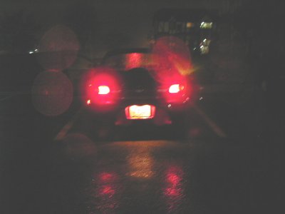 1997 Ford Taurus - A dark sedan is seen from the rear at night, with its brake lights illuminated and reflecting on the wet road surface.