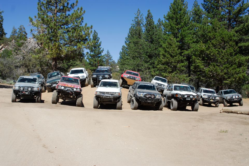 multiple modified SUVs parked on a dirt road with trees in the background