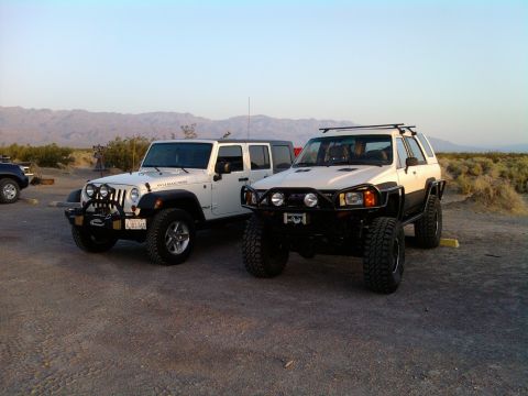 1985 Toyota 4Runner - Two modified SUVs, a Jeep and a Toyota, are parked in a desert landscape under a clear sky.